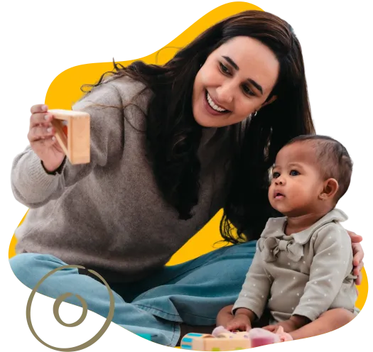 lady wearing gray sweatshirt holding up a block for an infant